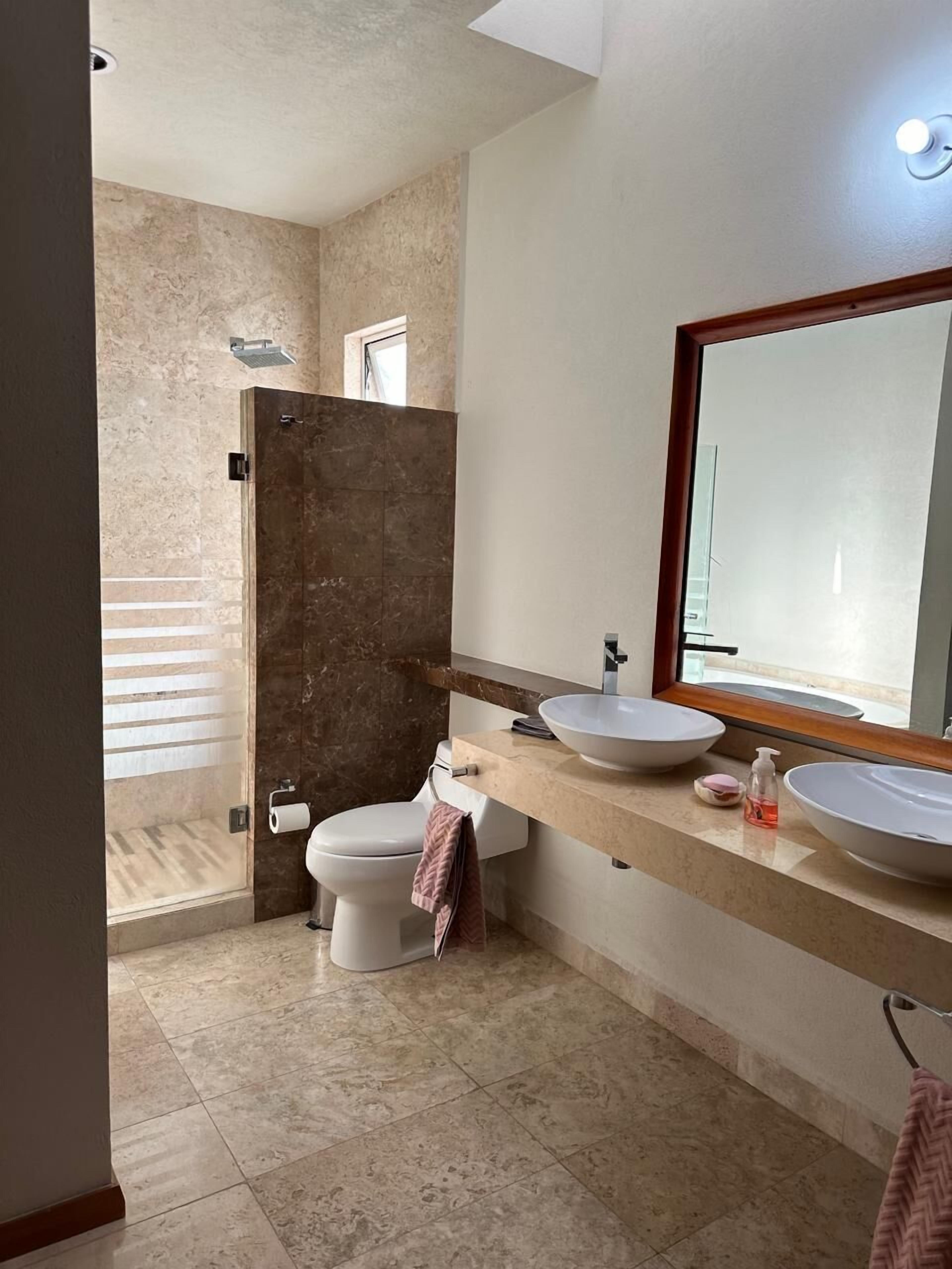 Une salle de bain moderne avec un grand miroir, deux lavabos, des toilettes et un espace douche.