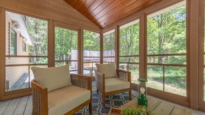 A sunroom with large windows, two wicker sofas, a patterned rug, and a table with a green lamp and plants. - Relax at Pier Cove Chalet: a cozy Boho 2-bedroom retreat in Fennville, MI. (Fennville)