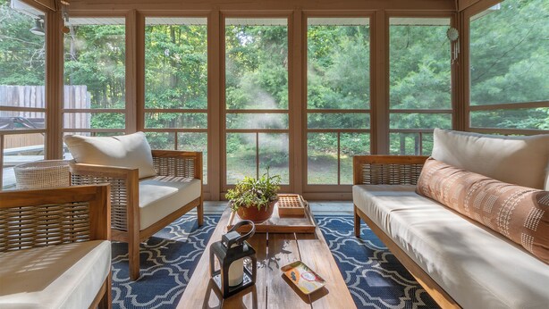 A sunroom with large windows, wicker furniture, and a central table with a plant. - Relax at Pier Cove Chalet: a cozy Boho 2-bedroom retreat in Fennville, MI. (Fennville)