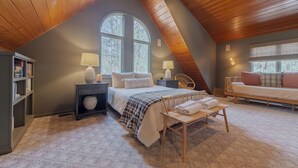 A cozy attic bedroom with a large bed, two bedside tables with lamps, a reading chair, and a small table with towels. - Relax at Pier Cove Chalet: a cozy Boho 2-bedroom retreat in Fennville, MI. (Fennville)