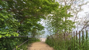 A concrete pathway leading to a beach, surrounded by lush greenery and a wooden fence. - Relax at Pier Cove Chalet: a cozy Boho 2-bedroom retreat in Fennville, MI. (Fennville)