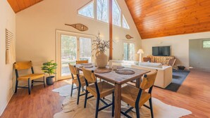 A spacious living area with a wooden ceiling, a dining table with chairs, a sofa, and a TV. - Relax at Pier Cove Chalet: a cozy Boho 2-bedroom retreat in Fennville, MI. (Fennville)