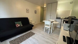 Een knus woongedeelte met een zwarte bank, een eettafeltje en een kitchenette.