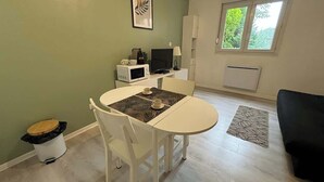 Een kleine, schone kamer met een eettafel, stoelen, een magnetron, een televisie en een radiator.