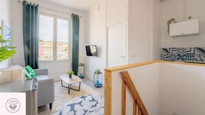 A modern living room with a sofa, coffee table, and a view of the city through large windows. - Le duplex inverse, Bollaert, Fac, gare, 2pers (Lens)