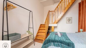A bedroom with a wooden staircase, a bed with a teal blanket, a small shelf with a plant, and a black metal bed frame. - Le duplex inverse, Bollaert, Fac, gare, 2pers (Lens)
