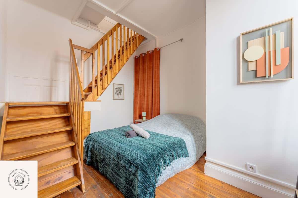 Ein Schlafzimmer mit einer Holztreppe, einem Bett mit einer türkisfarbenen Decke und einem gerahmten abstrakten Kunstwerk an der Wand.