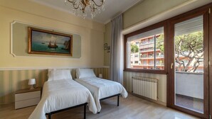 Ein Zimmer mit zwei Betten, einer Kandelaber, einem Gemälde, einem Fenster mit Blick auf Gebäude und einer Heizung.