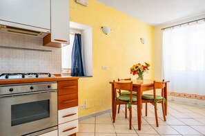 A kitchen with a stove, oven, and wooden cabinets. There is a dining table with chairs and a vase of flowers. - Bright 58 sqm apartment, perfect for 3 people, located 700 meters from the center of Riomaggiore, where you can appreciate the true flavors and colors of the Mediterranean in the heart of the 5Terre! The apartment boasts a splendid terrace overlooking th (Riomaggiore)
