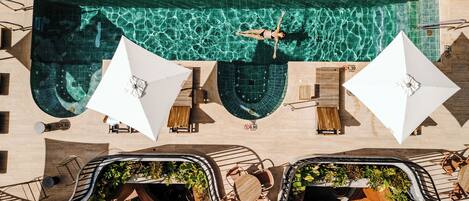 Vista aérea de una piscina con agua cristalina, rodeada de tumbonas y sombrillas, y una terraza curvada con vegetación.