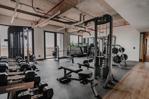 Un gimnasio con diversos equipos de ejercicio, incluyendo mancuernas, un banco y máquinas de pesas.