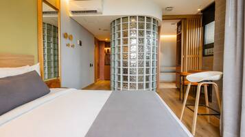 Una habitación de hotel con una cama, un taburete, un separador de vidrio y un armario de madera.