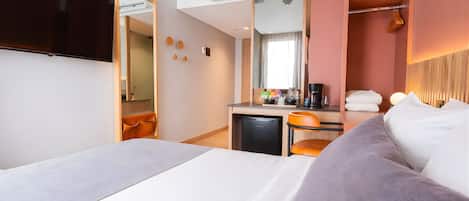 A hotel room with a bed, a desk with a coffee maker, a mirror, and a TV.