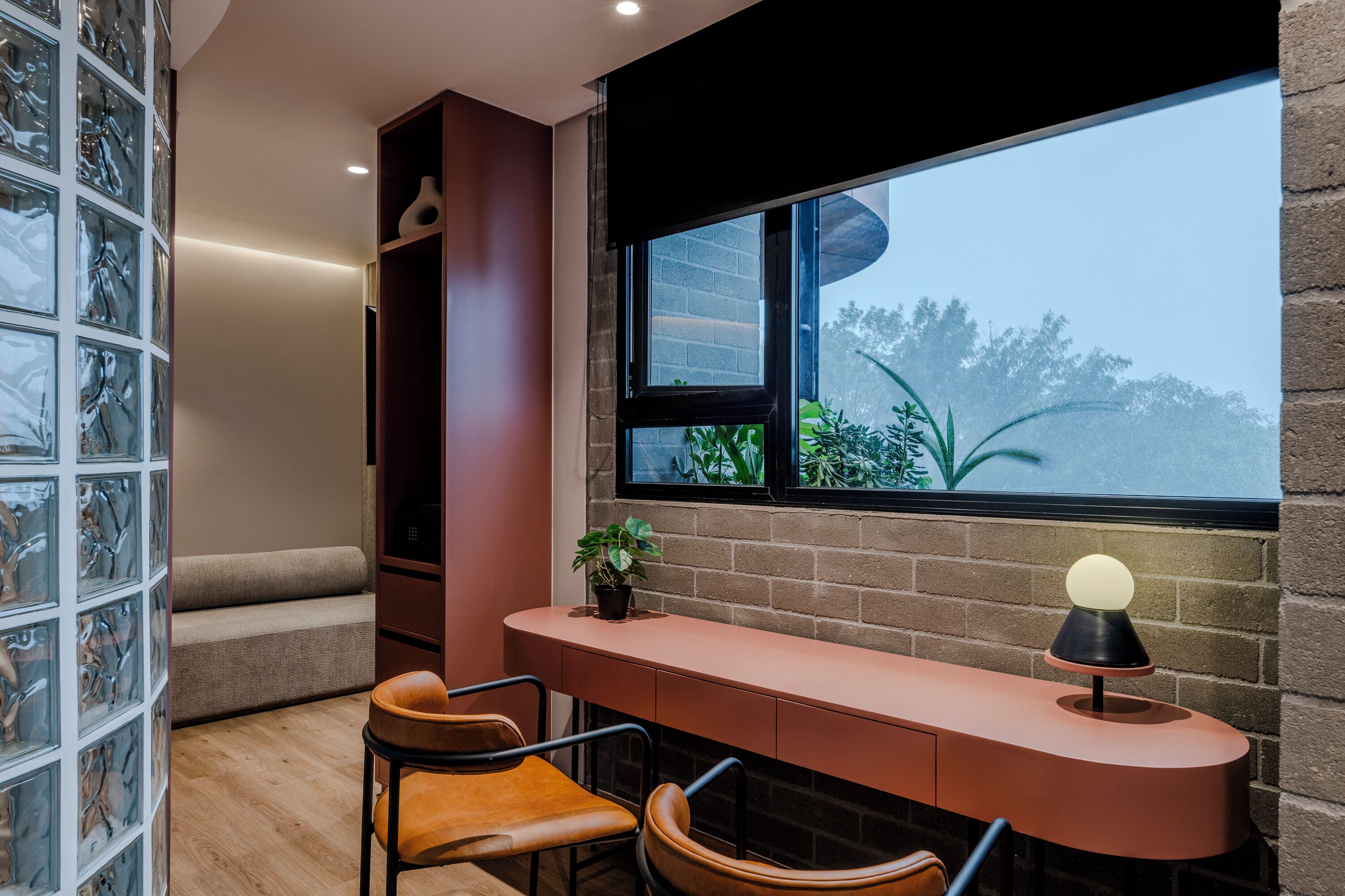A modern room with a curved desk, two chairs, a potted plant, and a large window with a view of greenery.