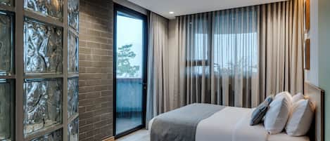 A modern bedroom with a large bed, a glass door leading to a balcony, and a brick wall.