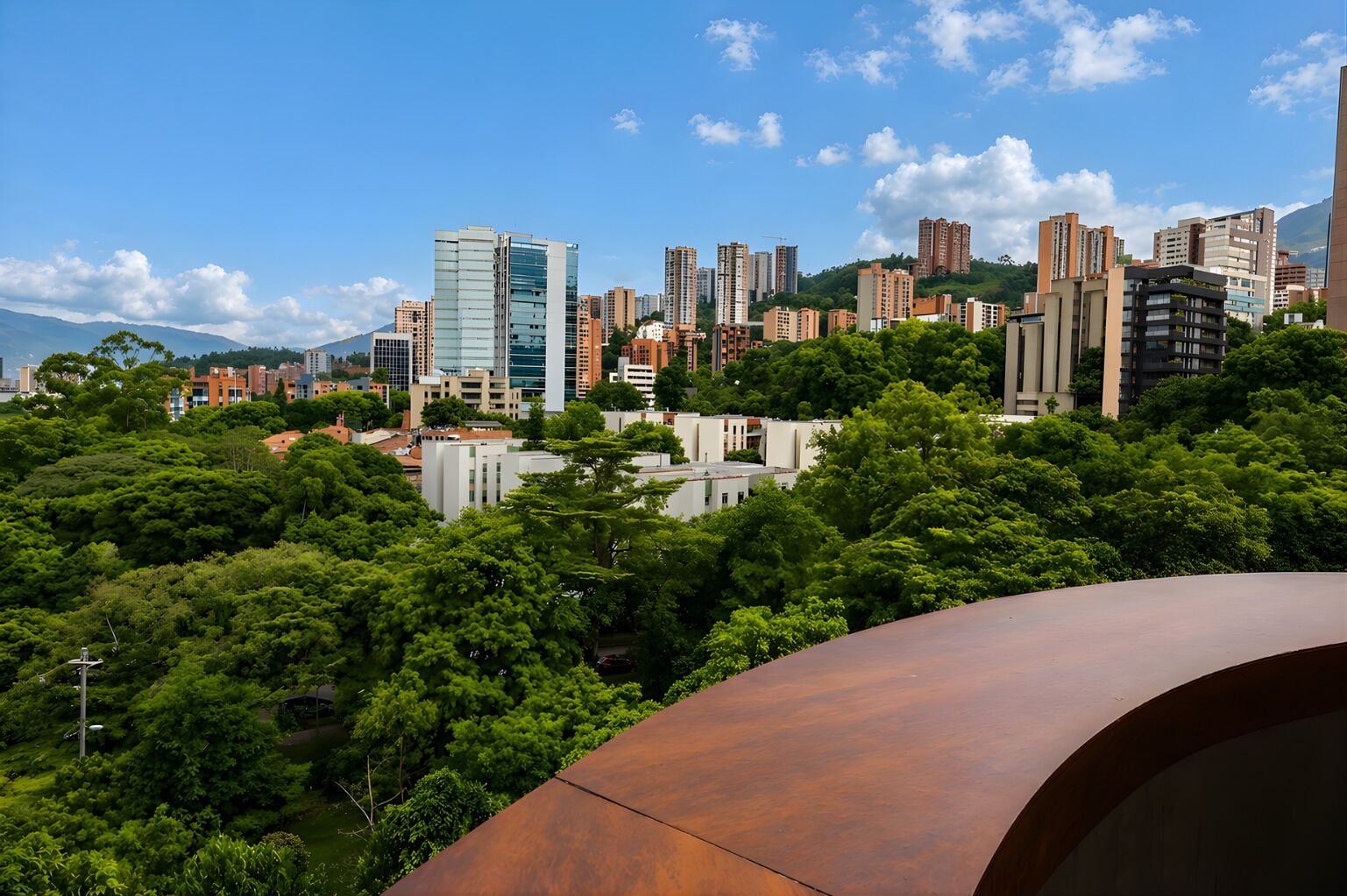 A cityscape with high-rise buildings, dense greenery, and a clear sky.