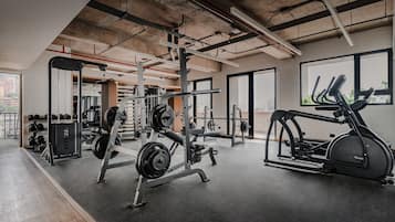 Un gimnasio con equipamiento de levantamiento de pesas, máquinas de cardio y un amplio ventanal que proporciona luz natural.