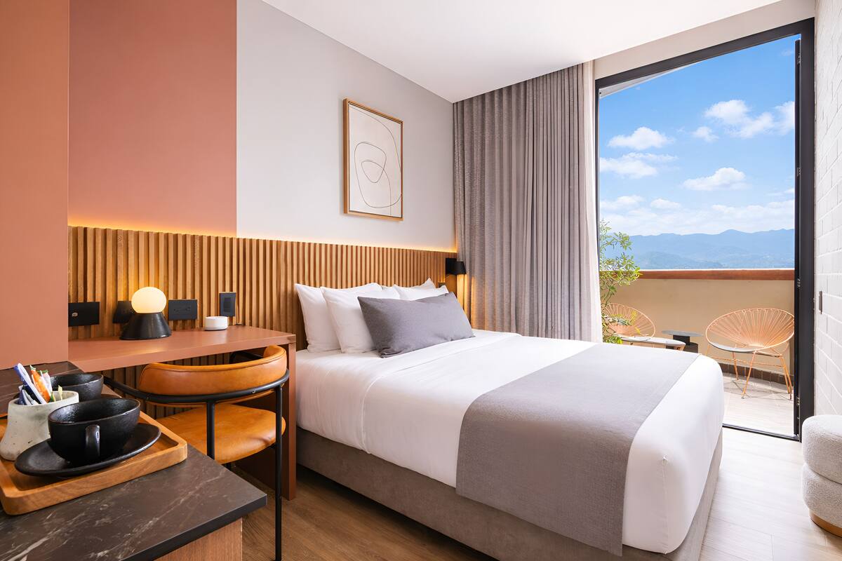 A modern hotel room with a bed, a desk, a chair, and a balcony with a view.