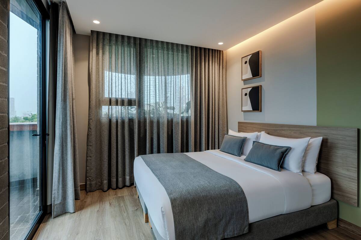 A modern hotel room with a large bed, a view through sheer curtains, and a balcony.