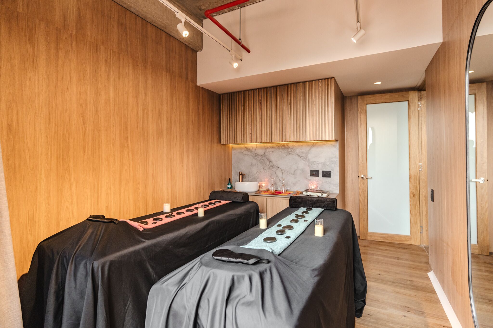 Une salle de spa moderne avec des murs en bois, une table de massage surmontée de marbre et un petit espace d’accueil doté d’un mur en marbre et d’une bouteille d’eau.