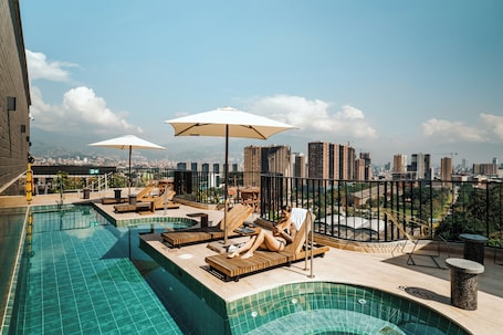 Una piscina al aire libre, sombrillas, sillones reclinables de piscina