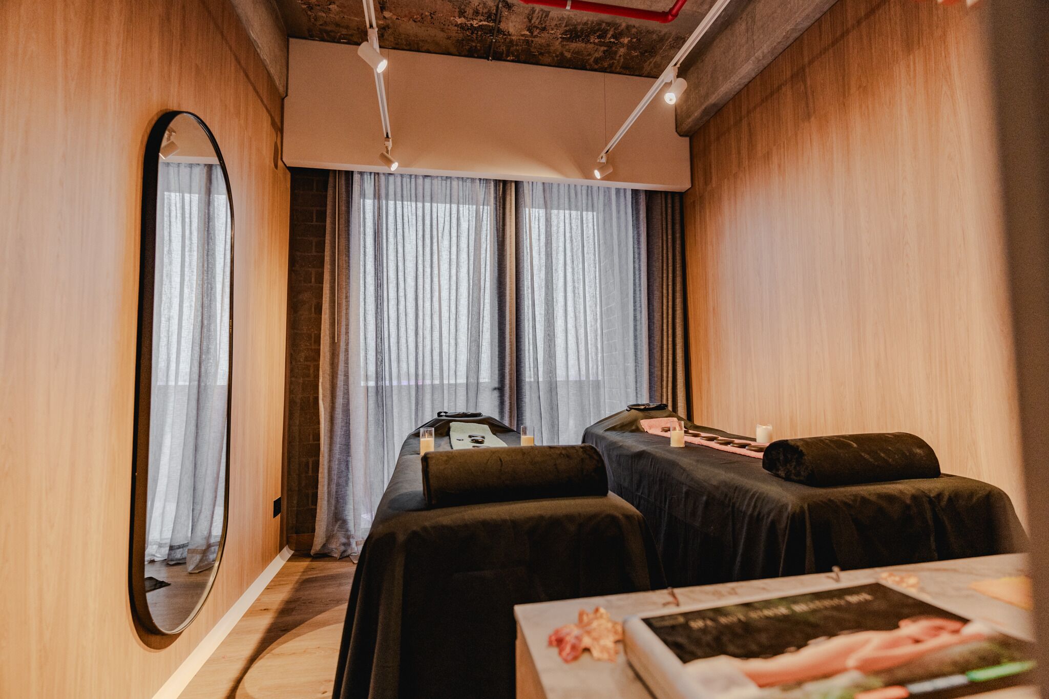 Une pièce moderne avec un grand miroir, deux tables de massage et une petite table sur laquelle est posé un magazine.