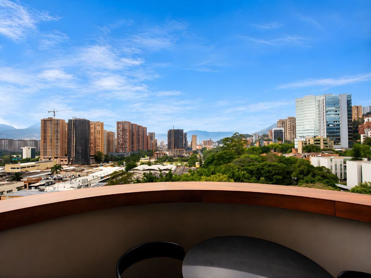 A cityscape with high-rise buildings, a clear sky, and a balcony with chairs.