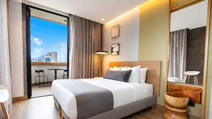 A hotel room with a large bed, a wooden headboard, a bedside table, a mirror, and a view of the cityscape. - Heiss Hotel By Jalo (Medellín)