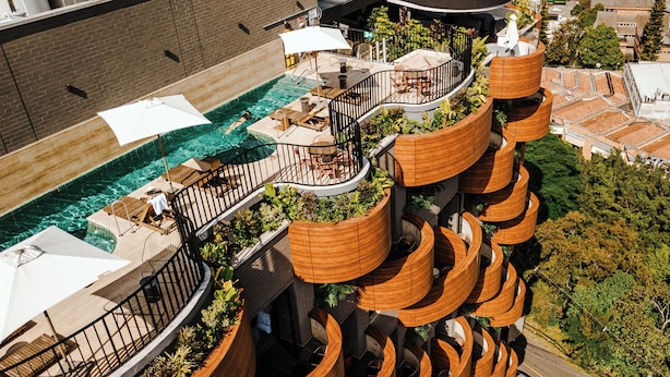 A multi-level outdoor pool area with tiered wooden structures, lounge chairs, and umbrellas. - Heiss Hotel By Jalo (Medellín)