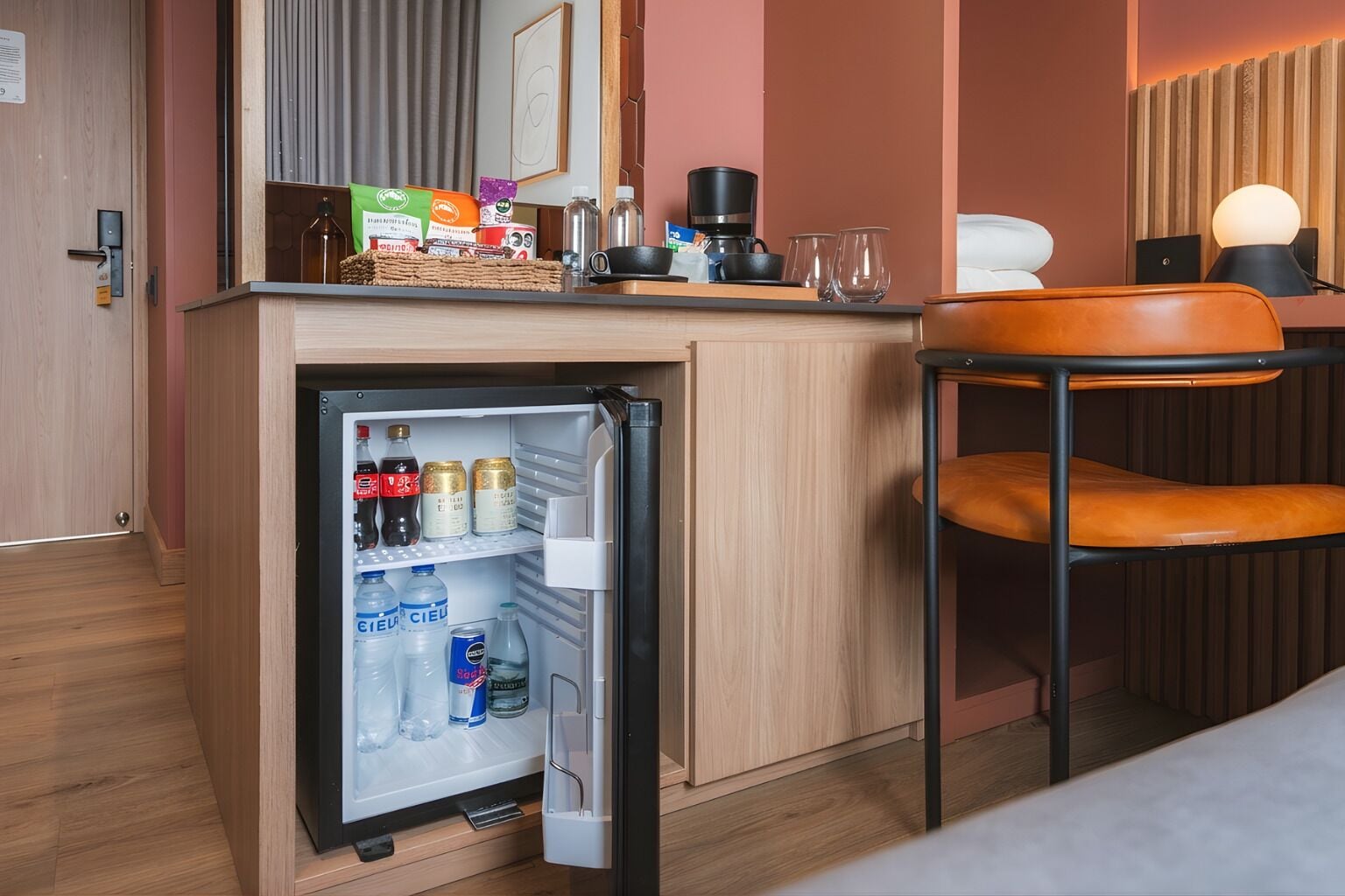 A compact kitchenette with a refrigerator, a coffee maker, and a small dining area with a chair.