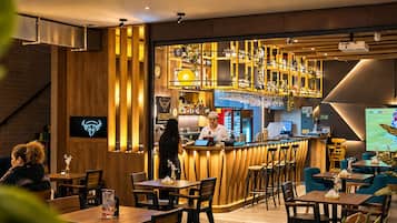 Una zona de bar con detalles de madera, un barman y una pantalla mostrando un evento deportivo.