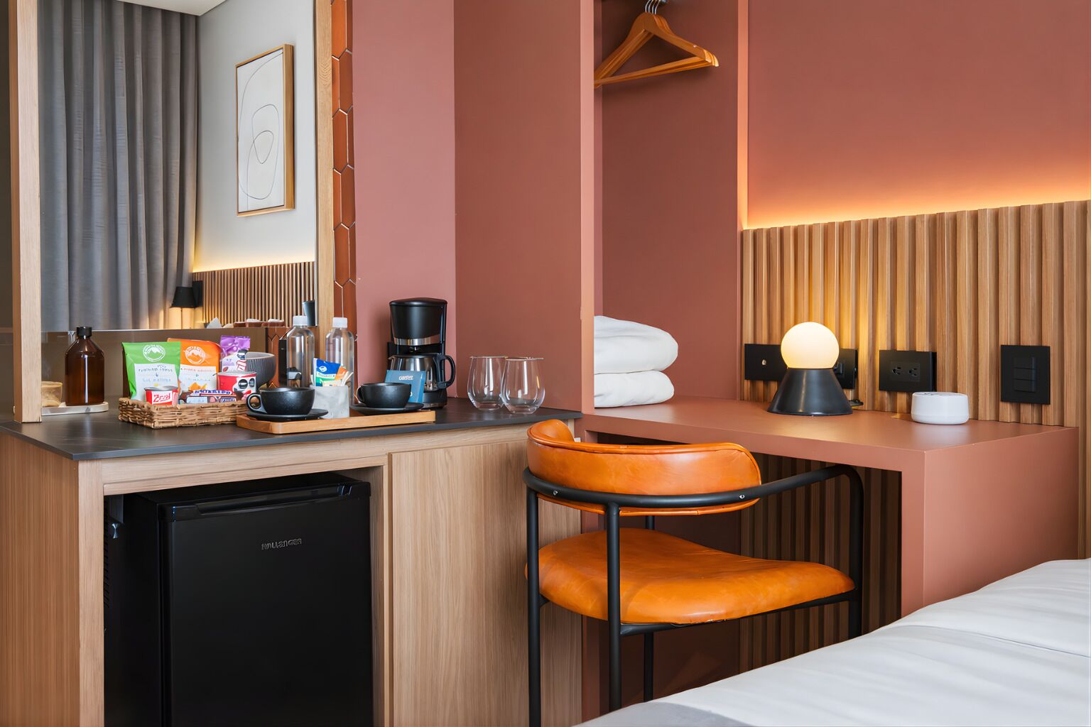 Et kompakt hotelværelse med tekøkken, seng, skrivebord med stol og et knagered.