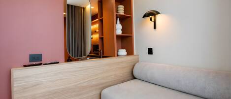 A modern room with a wooden console, a round mirror, a sofa, and a wall-mounted lamp.