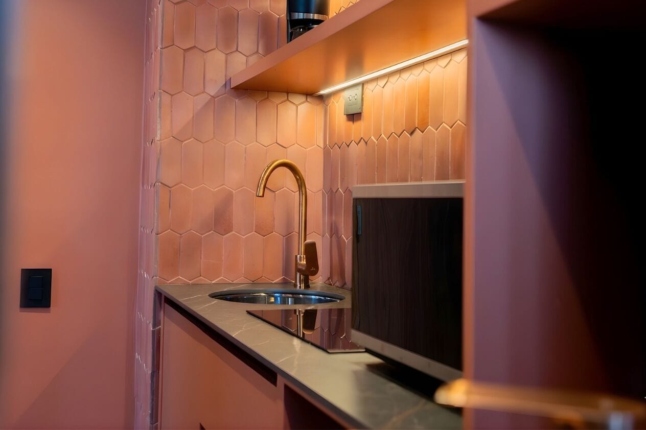 Una cocina moderna con salpicadero de azulejos hexagonales, pileta de acero inoxidable y una lámpara de pared.