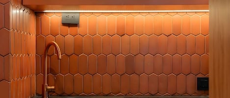Una cocina con salpicadero de azulejos hexagonales, un grifo de cobre y una máquina de café.