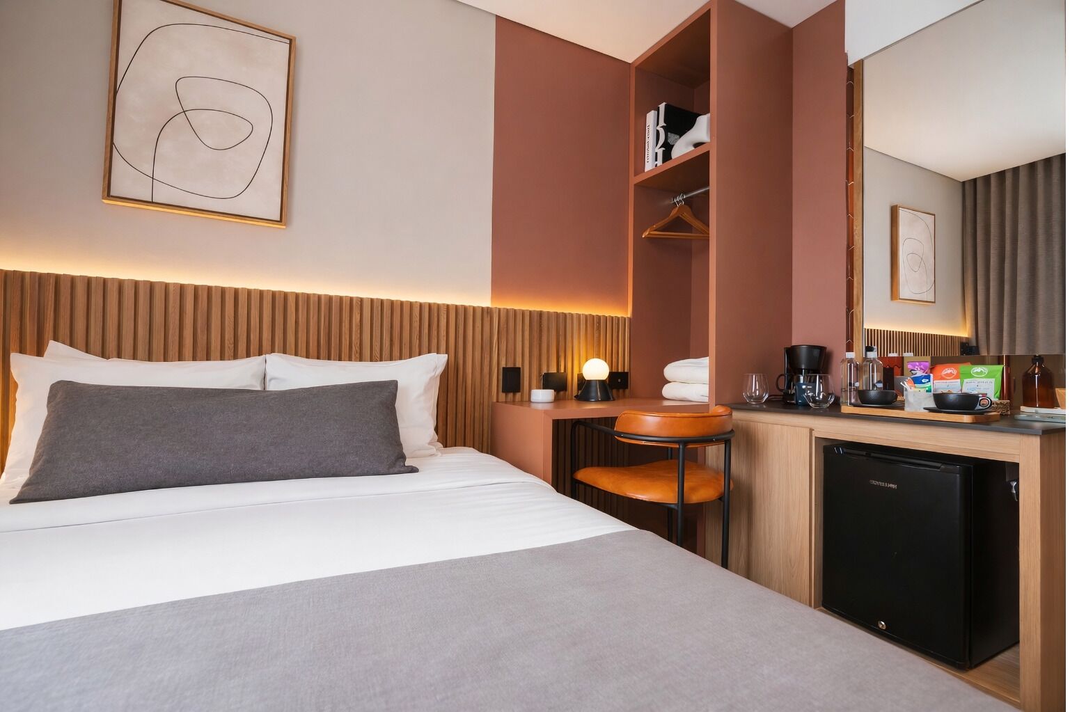 A hotel room with a bed, a desk with a coffee maker, a chair, and a small kitchenette.
