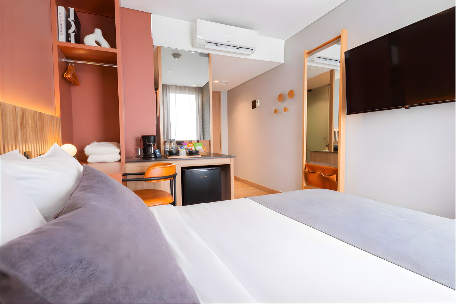 A hotel room with a bed, a desk with a coffee maker, a TV, and a wardrobe.