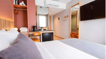 A hotel room with a bed, a desk with a coffee maker, a TV, and a wardrobe.