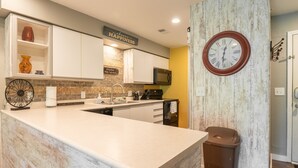 Une cuisine moderne avec des meubles blancs, un plan de travail en marbre, une horloge et une poubelle.