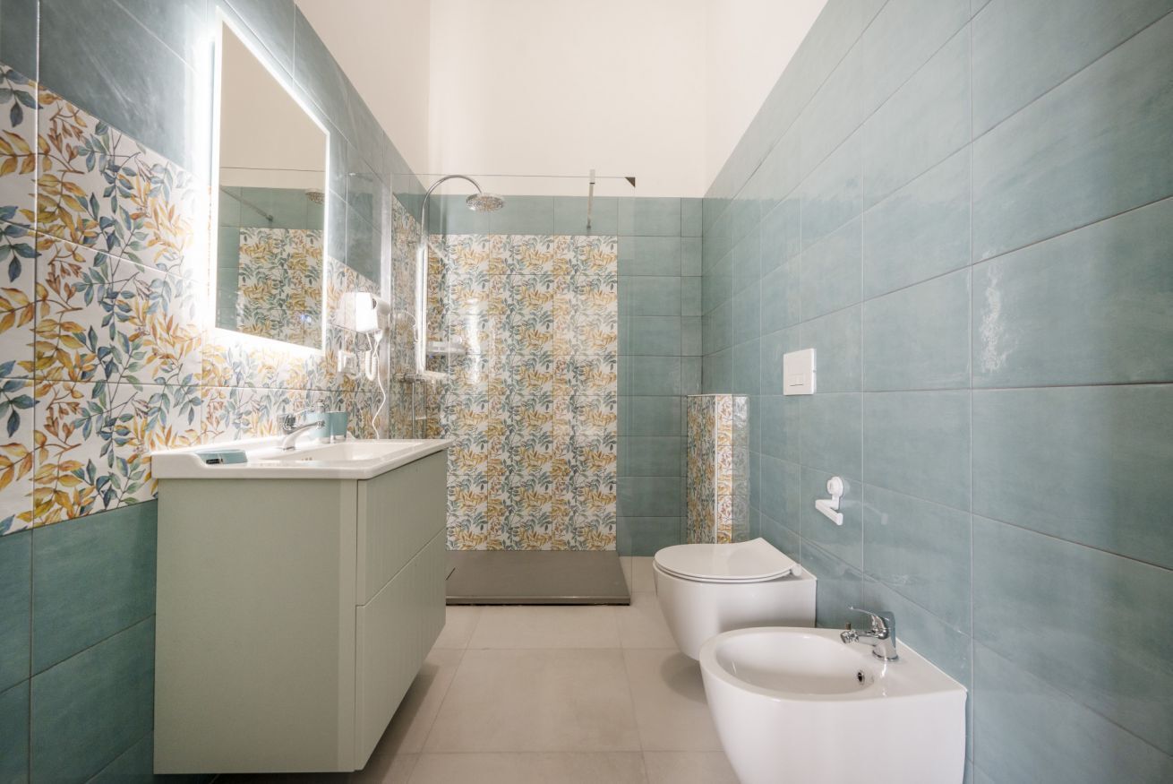 A bathroom with a sink, toilet, and shower area, featuring a large mirror and tiled walls.