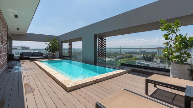 Un área de piscina en la azotea con terraza de madera, sillas de descanso y vistas a la ciudad.