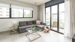 Un moderno salón con un sofá gris, una mesa de centro de vidrio y vistas a un balcón con mobiliario exterior.