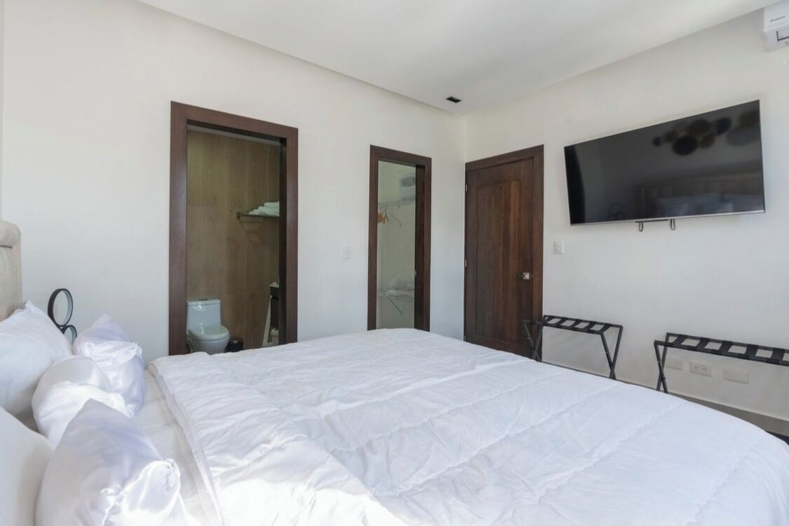 A hotel room with a bed, a TV mounted on the wall, and two doors.