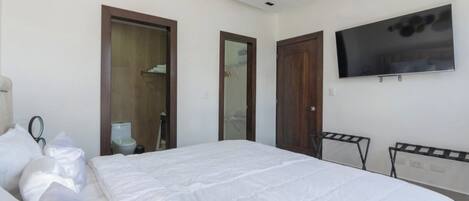 A hotel room with a bed, a TV mounted on the wall, and two doors.