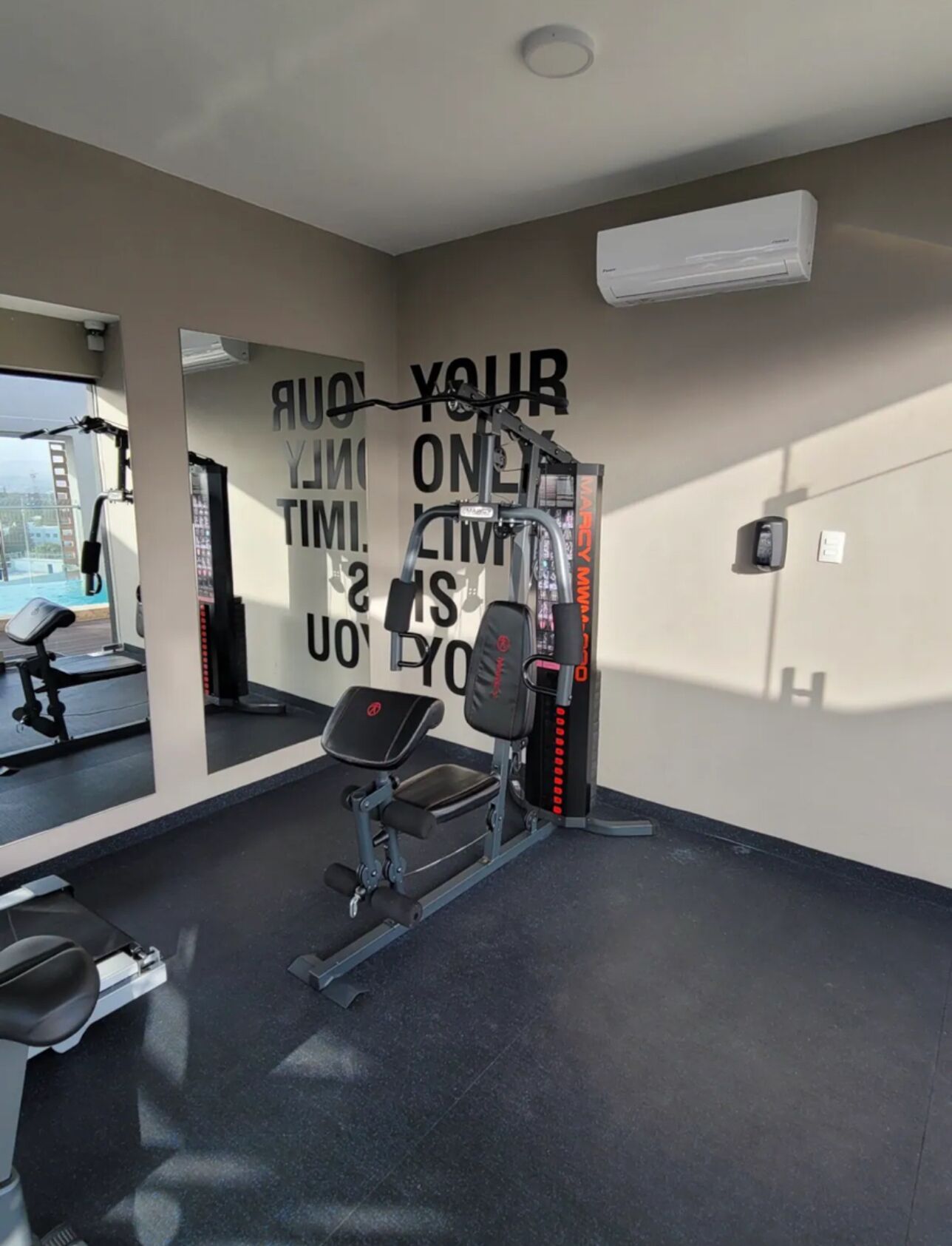 A gym with a wall-mounted mirror, a weight bench, and a squat rack.