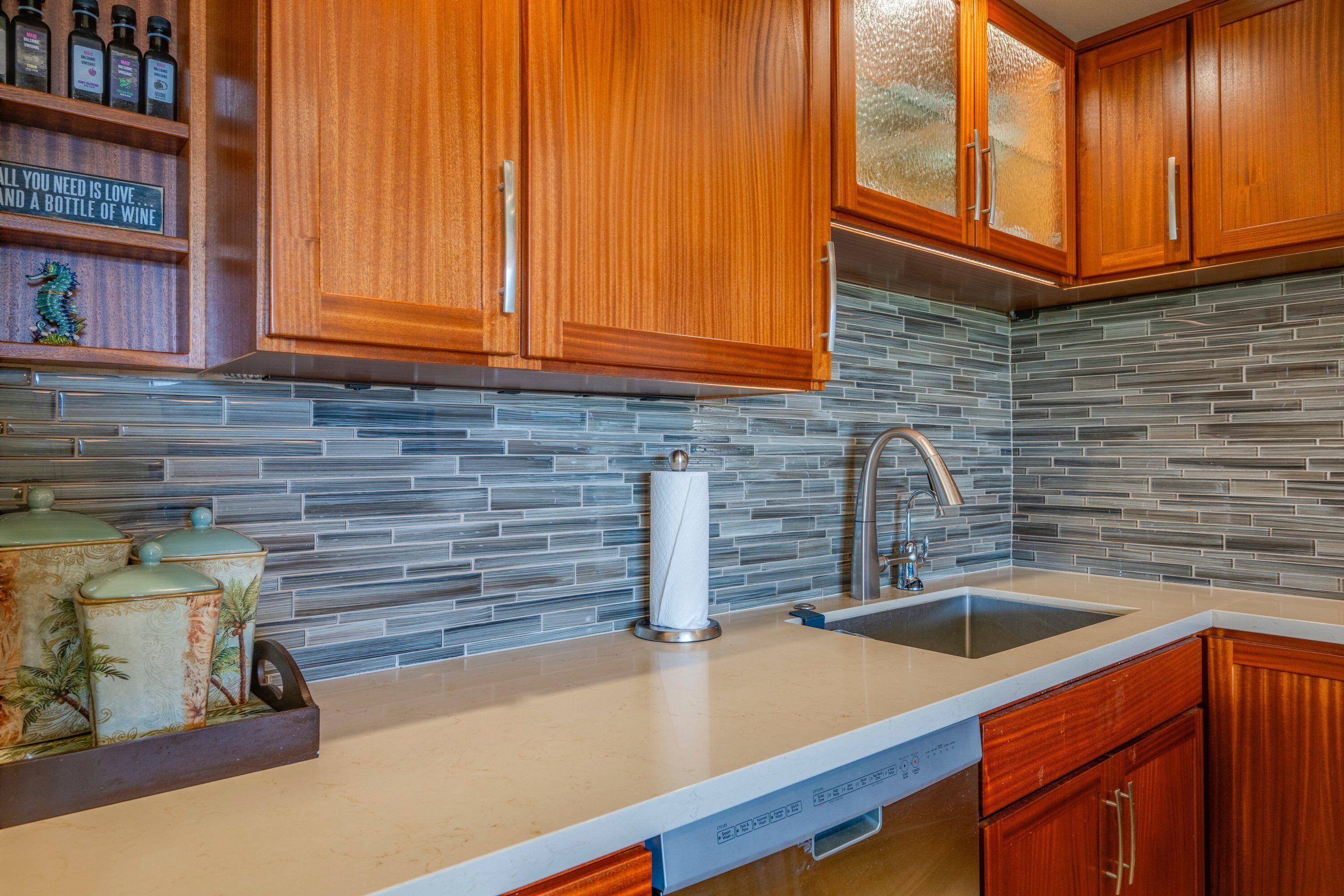 A kitchen with wooden cabinets, a tiled backsplash, a stainless steel sink, and a dish soap dispenser.