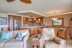 A modern kitchen with a central island, wooden cabinets, and a dining area with wicker furniture. - Oceanfront 2bd Maui Kihei getaway, stunning views (Kihei)