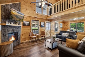 Interior acogedor de una cabaña con chimenea de piedra, paredes de madera, un balcón y un área de estar confortable.
