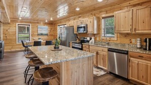 A spacious kitchen with wooden cabinets, granite countertops, stainless steel appliances, and a bar area with stools.