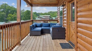 A wooden deck with a built-in sectional sofa and a small table, overlooking a forested area.